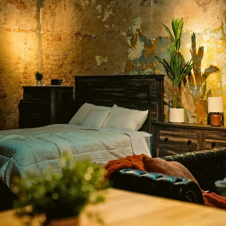 Cozy bedroom featuring a wooden bed, plush bedding, and plants against a textured wall.