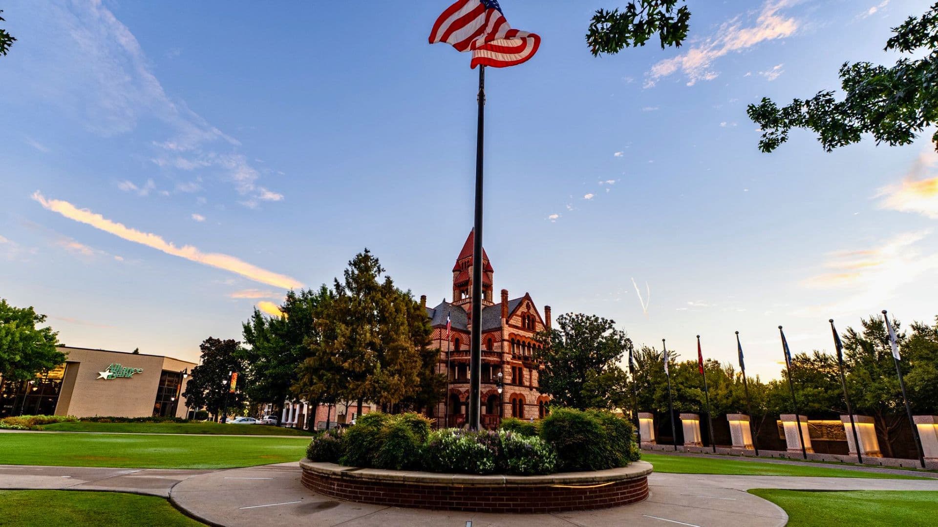A historic building with a flagpole and American flag surrounded by greenery in a park.