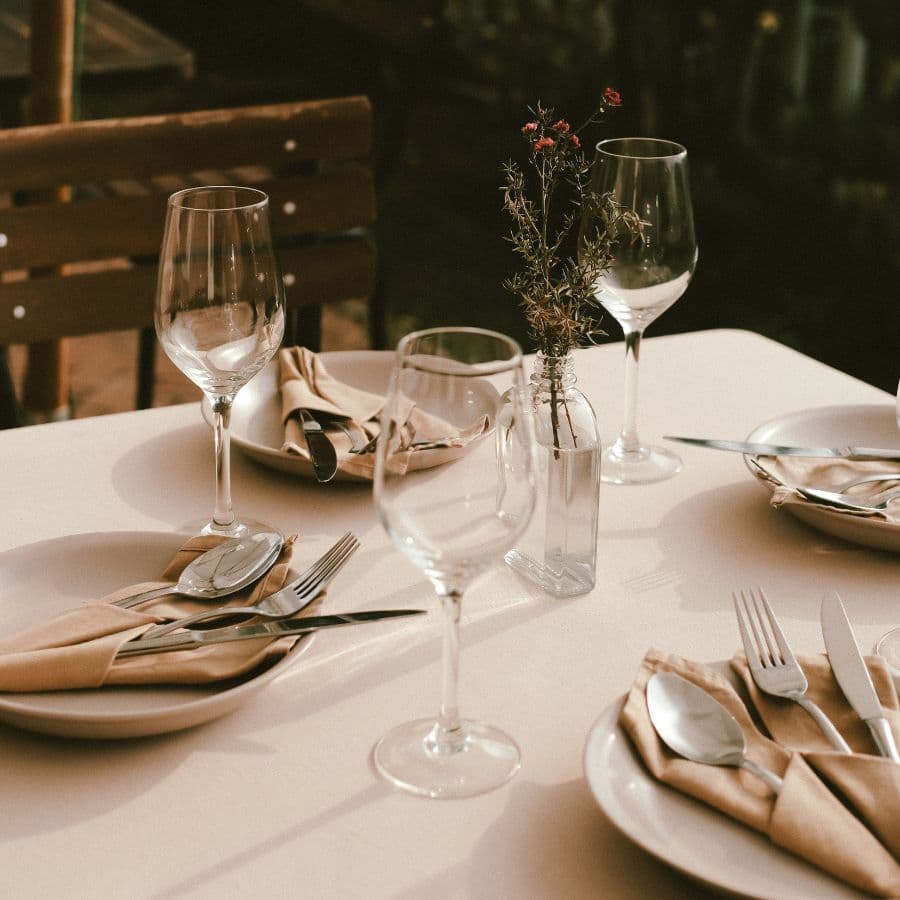 A beautifully set dining table with plates, cutlery, and glasses, accented by a small floral centerpiece.